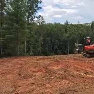 Two acres of cleared red clay ground with a mini excavator, ready for an orchard