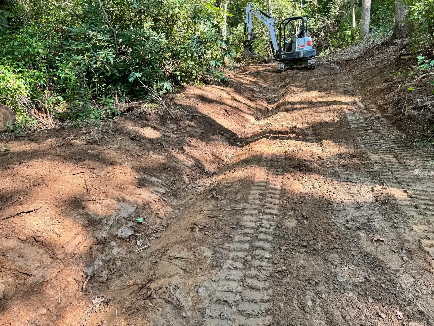 Steep road with a ditch and water break cut across it and a Bobcat mini excavator at the top