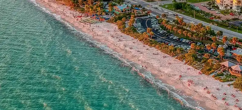 Golden-hour aerial of Barefoot Beach in Bonita Springs, with white sand, palm trees and turquoise Gulf water